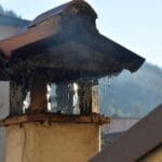 Ceglany komin kamienicy z dymem na tle miejskiej zabudowy