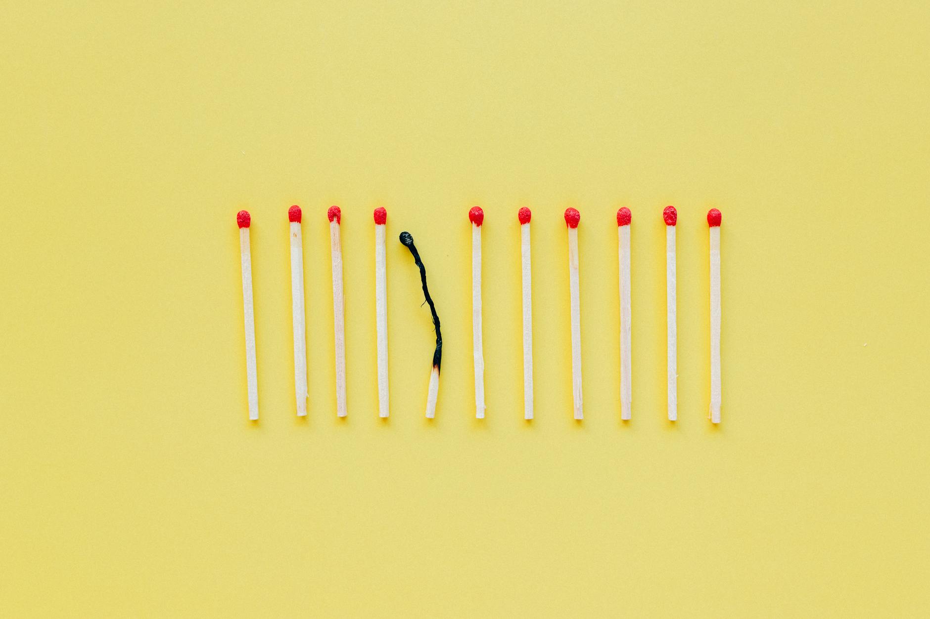 Zwęglona zapałka wśród nowych zapałek na żółtym tle