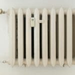 Biały metalowy grzejnik na tle jasnej ściany w minimalistycznym wnętrzu