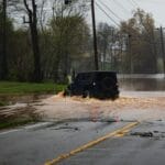 Samochód terenowy jedzie po zalanej deszczem drodze wśród drzew