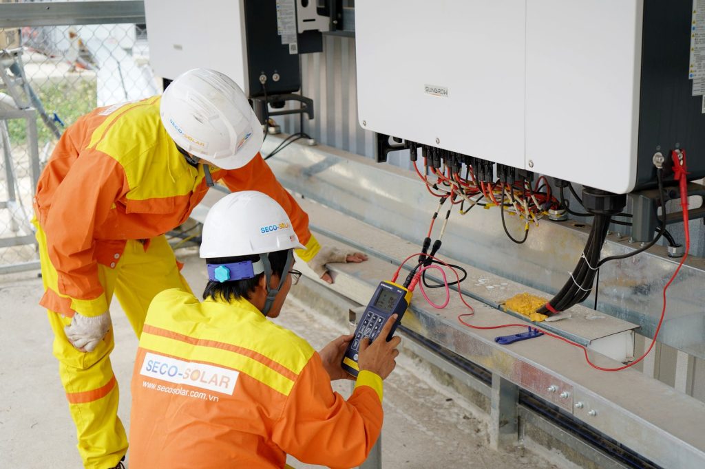 Dwóch elektryków instaluje i testuje system fotowoltaiczny na budowie